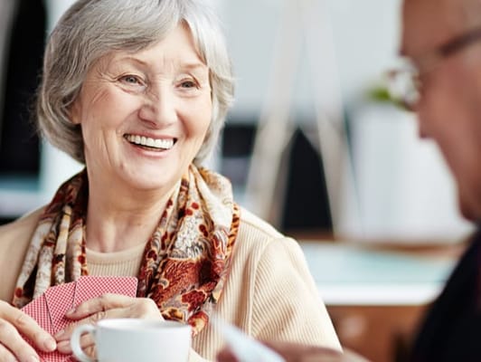 Senior woman smiling while playing cards with a companion