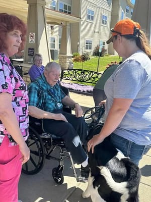 Residents interacting with a caregiver and a pet outdoors