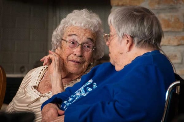 Two elderly women engaged in conversation indoors