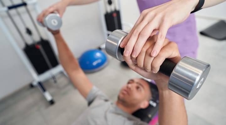 Resident lifting weights with staff assistance in a gym