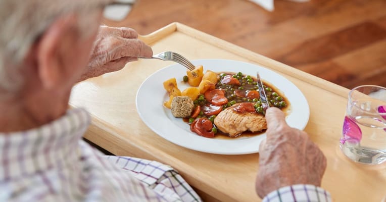 A resident enjoying a meal with chicken and vegetables
