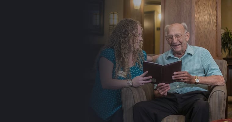 A resident and staff member reading together in a common area