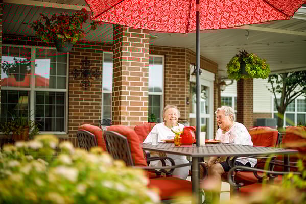 Two residents enjoying conversation under a patio umbrella