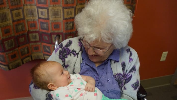 An elderly woman holding a baby, sharing joy.