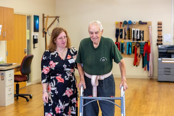 Staff assisting a resident with a walker in a therapy room