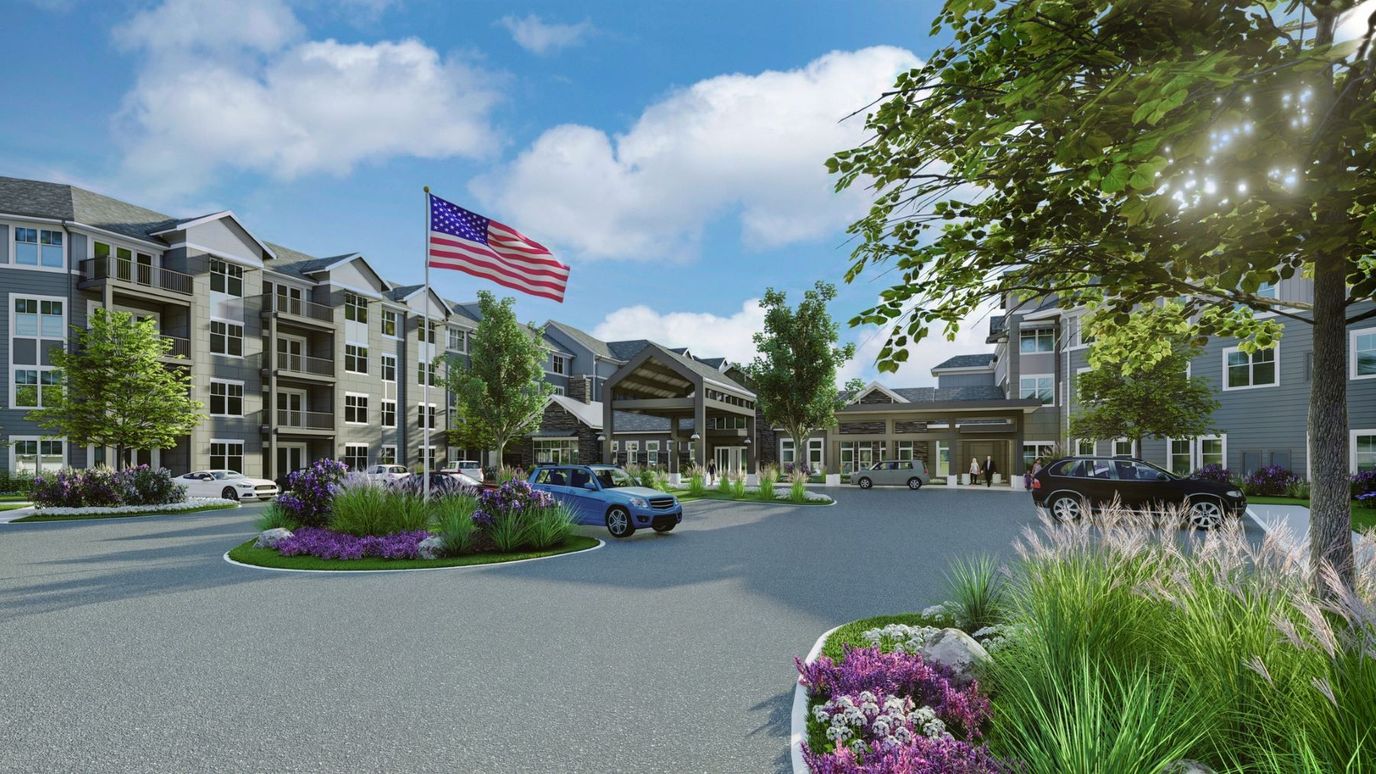 A landscaped entrance to Rivertown Ridge with flag and cars