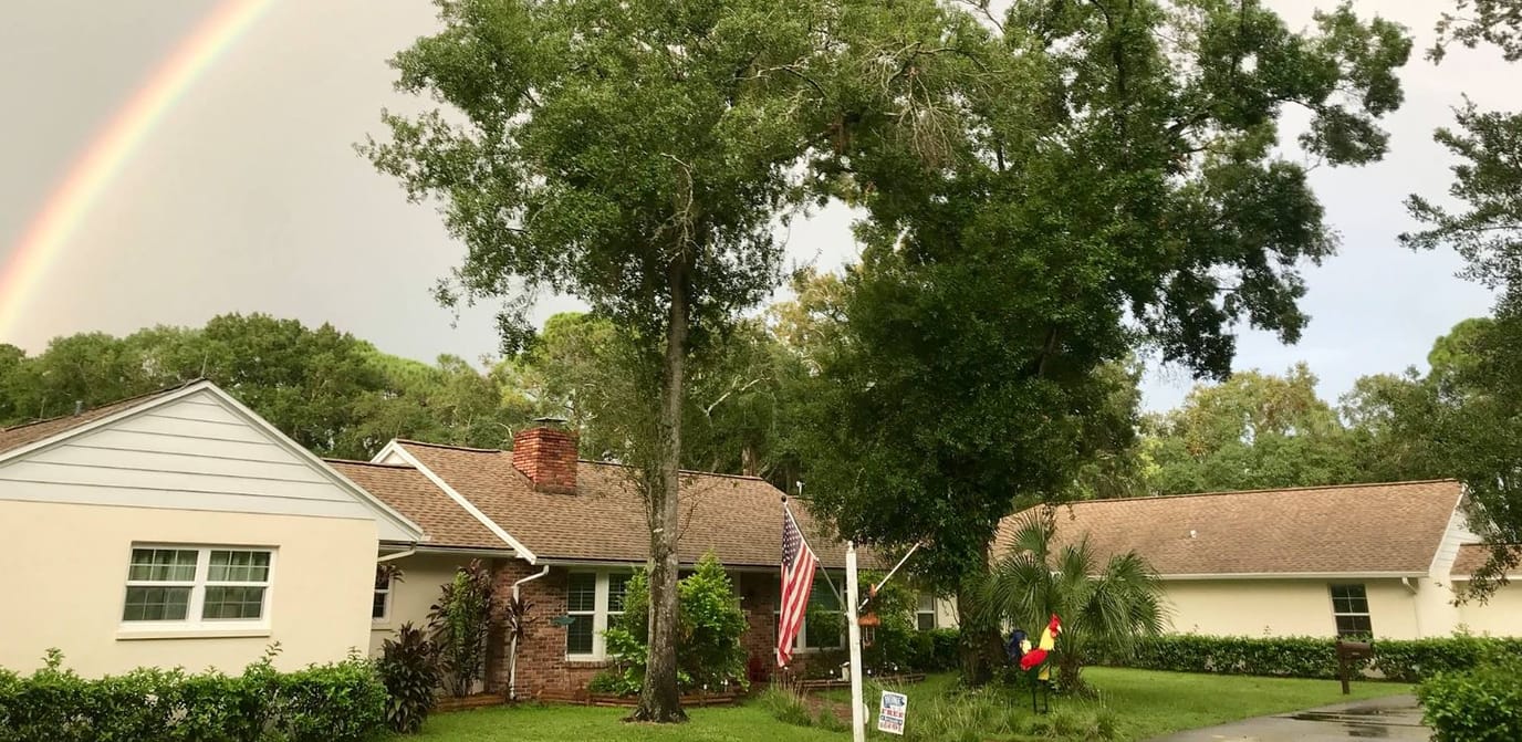 Exterior view of the assisted living facility with trees and a rainbow