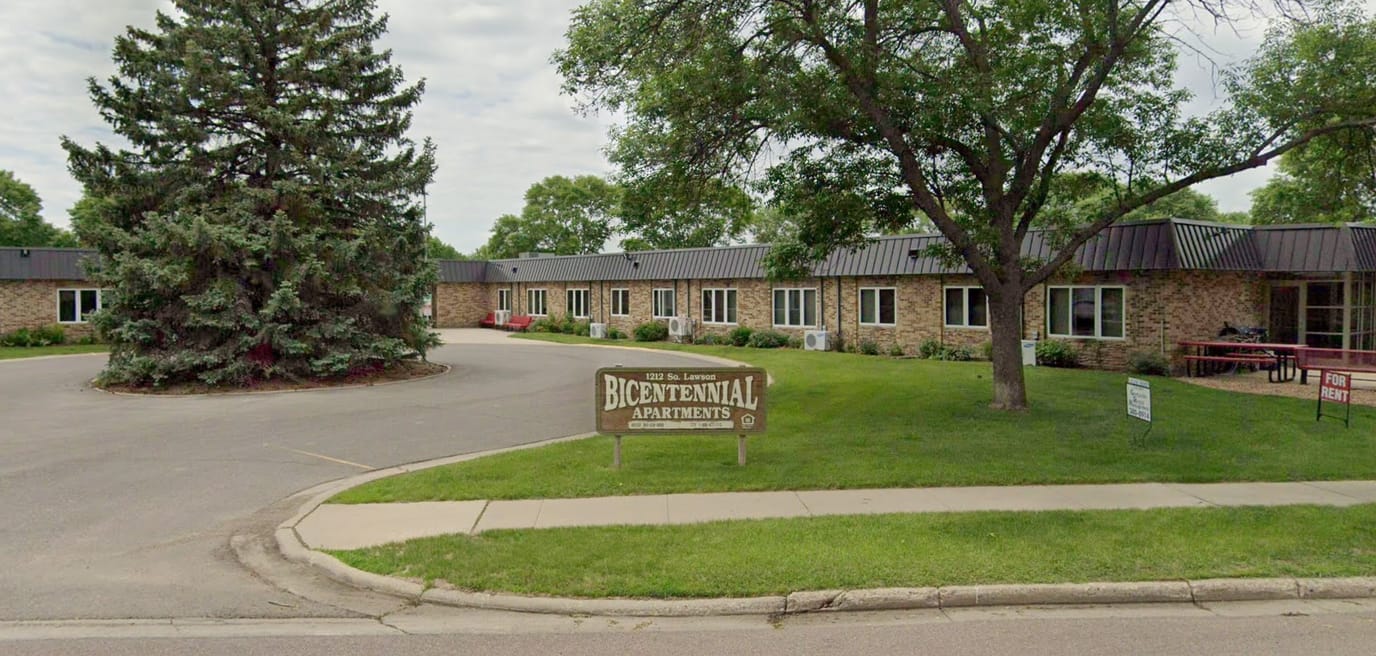 Exterior view of Bicentennial Apartments, featuring landscaping and signage