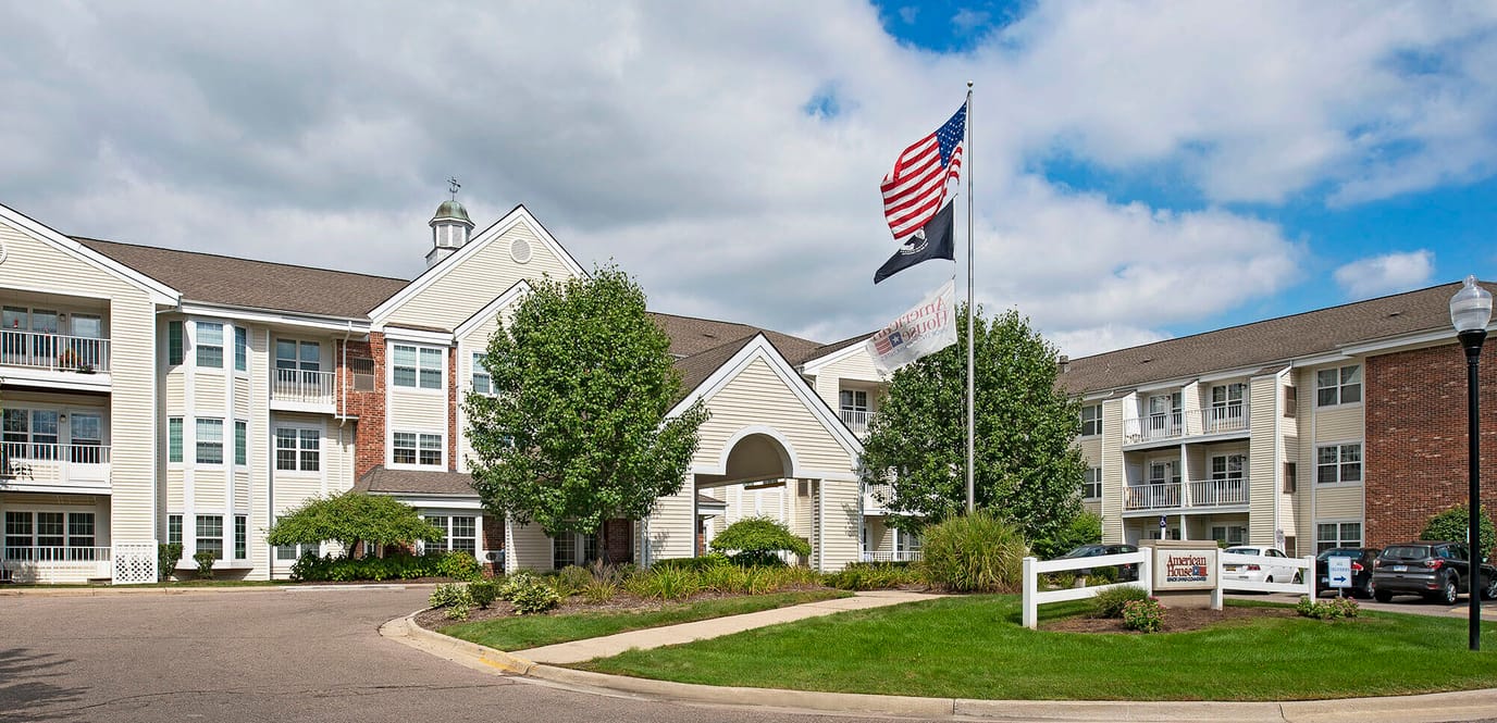 Exterior view of a senior living facility with flag and greenery
