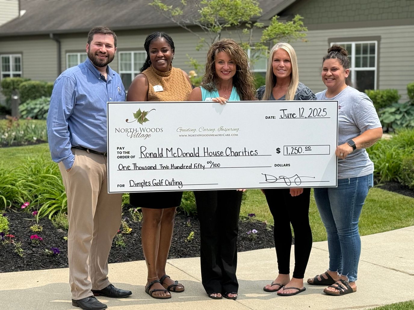 Staff presenting a large donation check outdoors.