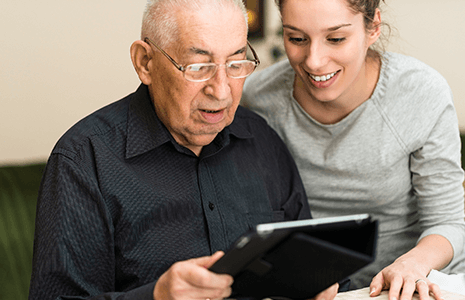 Elderly man and caregiver sharing a tablet.