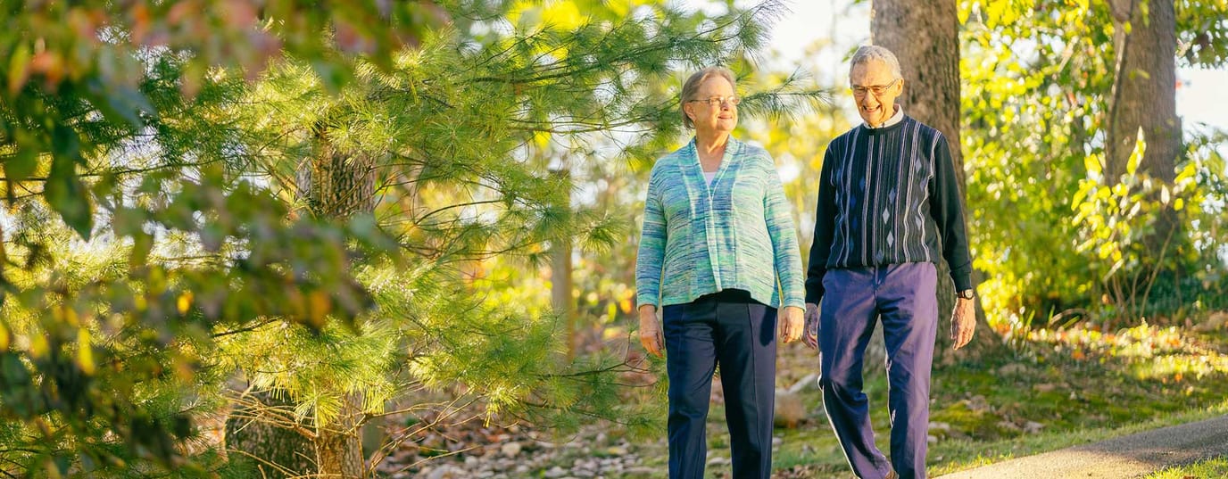 Two seniors walking along a pathway in nature.