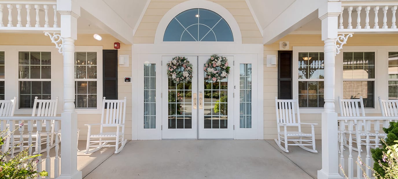 Entrance of a senior living facility with rocking chairs and floral decor