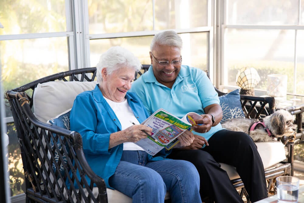 Elderly resident with caregiver enjoying a magazine