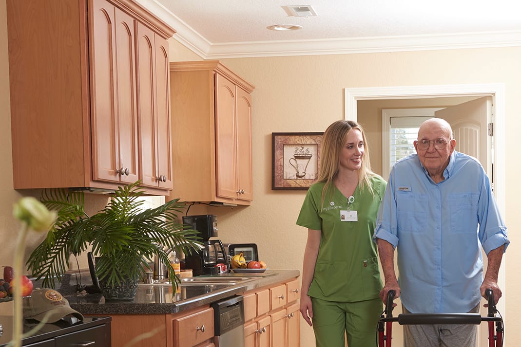 Staff assisting an elderly resident in a kitchen setting.