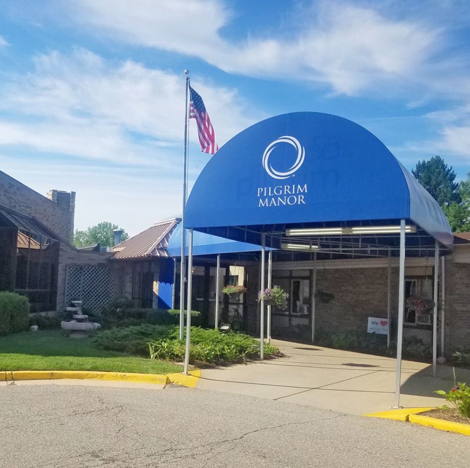 Entrance of Pilgrim Manor with a blue canopy and flag