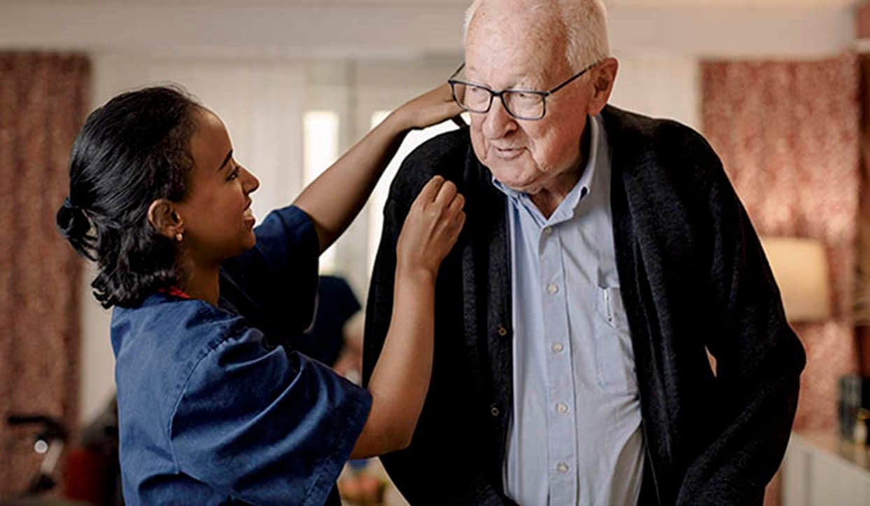 Caregiver assisting an elderly man indoors.