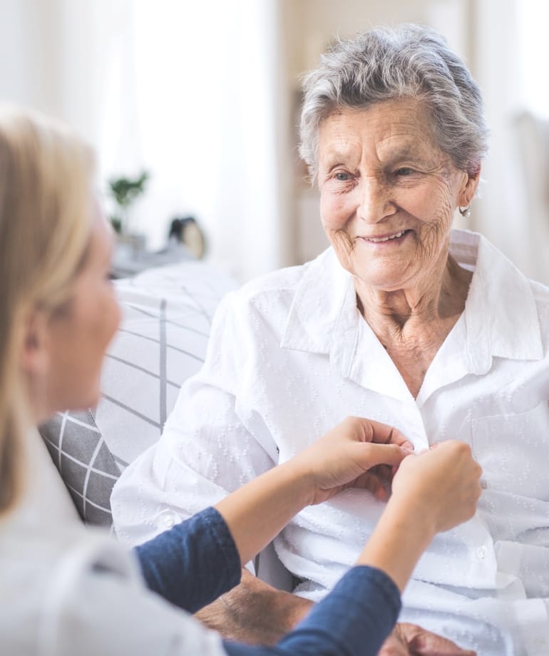 Caregiver assisting an elderly woman in a bright room.