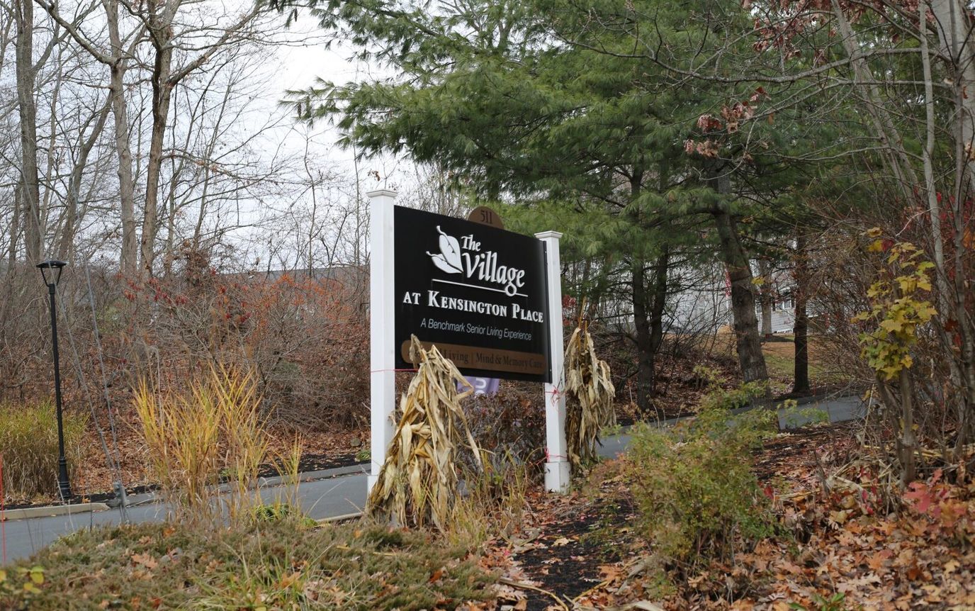 Sign for The Village at Kensington Place in a wooded area
