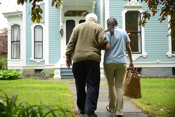 A caregiver assisting a senior outdoors near a house.