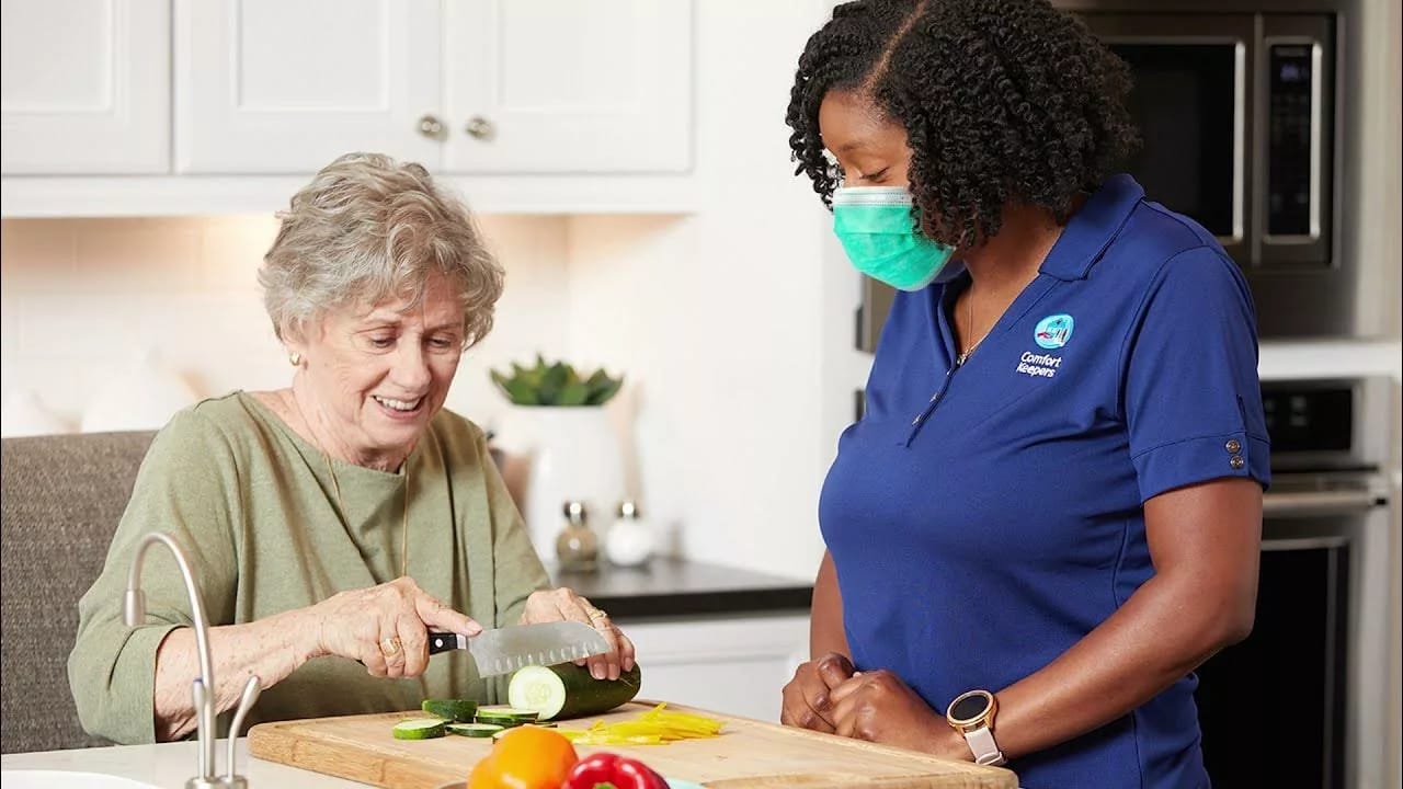 Senior resident and caregiver preparing vegetables in a kitchen.