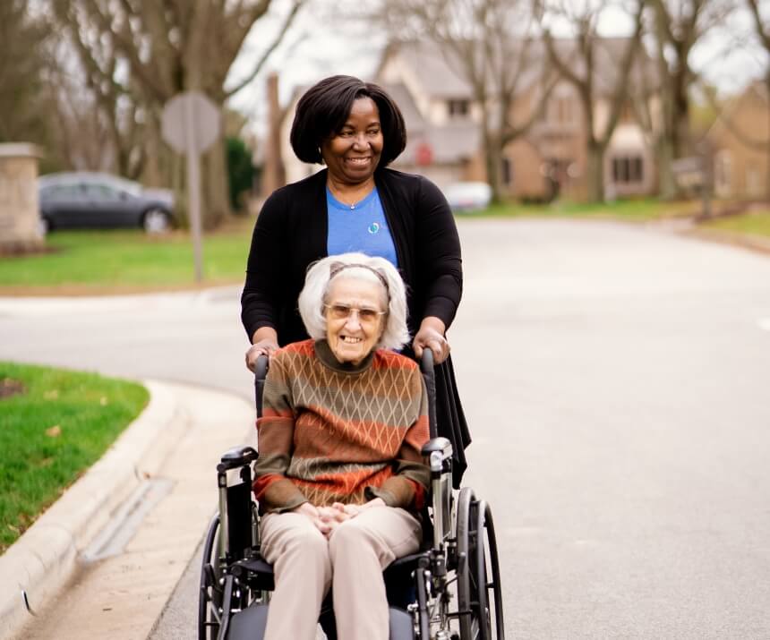 Caregiver assisting a resident in a wheelchair outdoors.