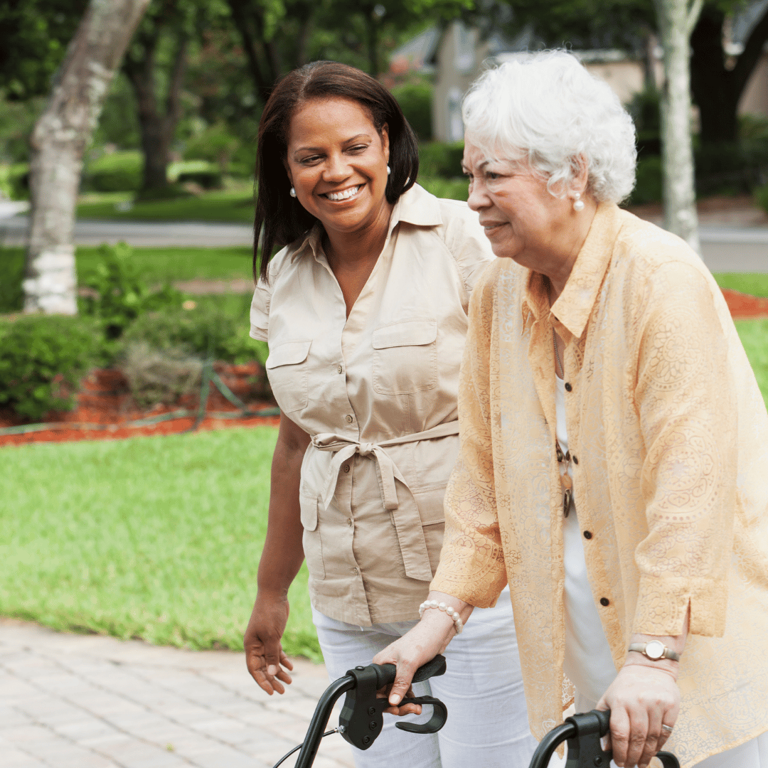 A caregiver assists an elderly woman outdoors.