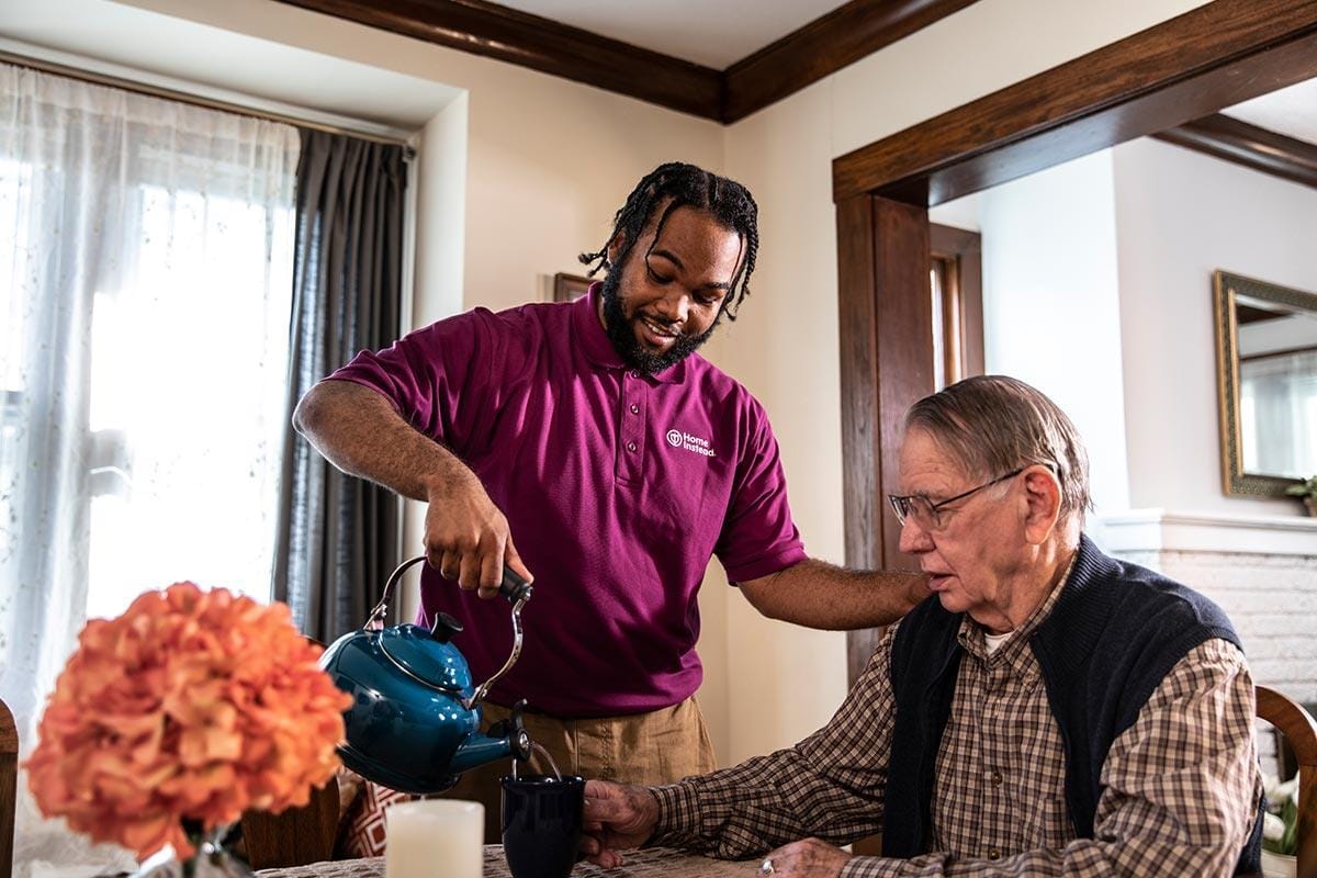 Caregiver pouring tea for a resident at a dining table