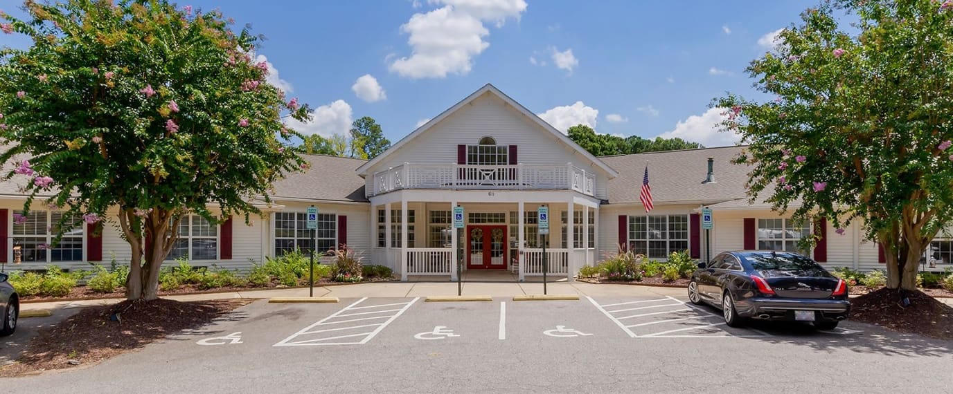 Exterior view of a senior living facility with parking and gardens