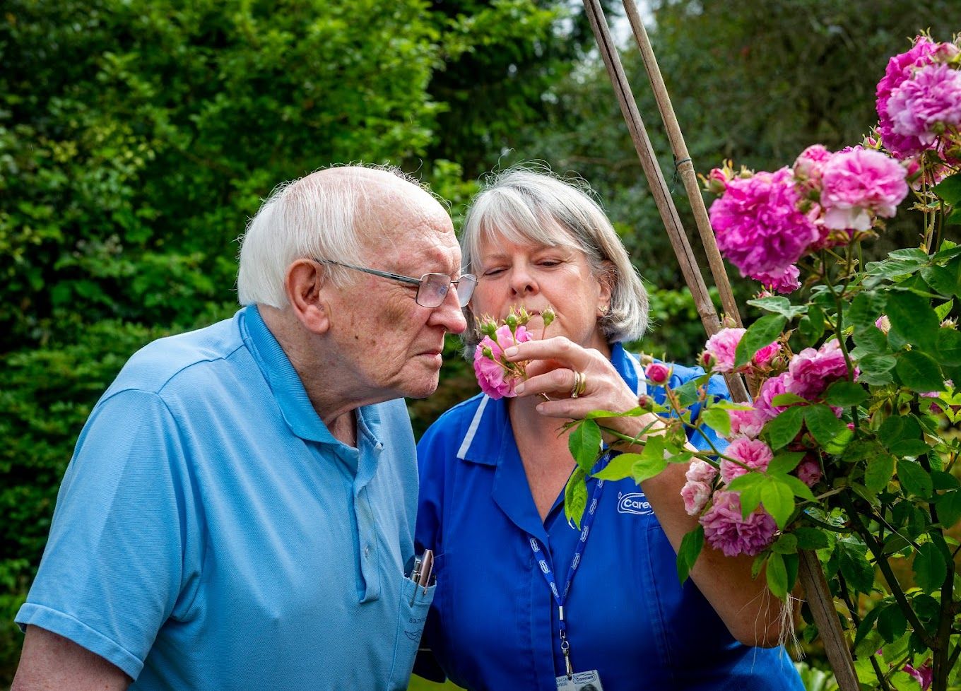 An elderly man smelling flowers with a staff member