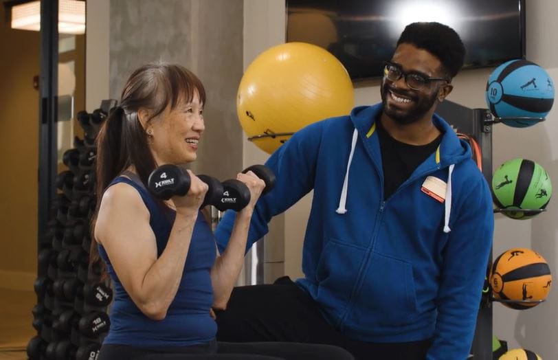 Senior resident lifting weights with trainer in a fitness area.
