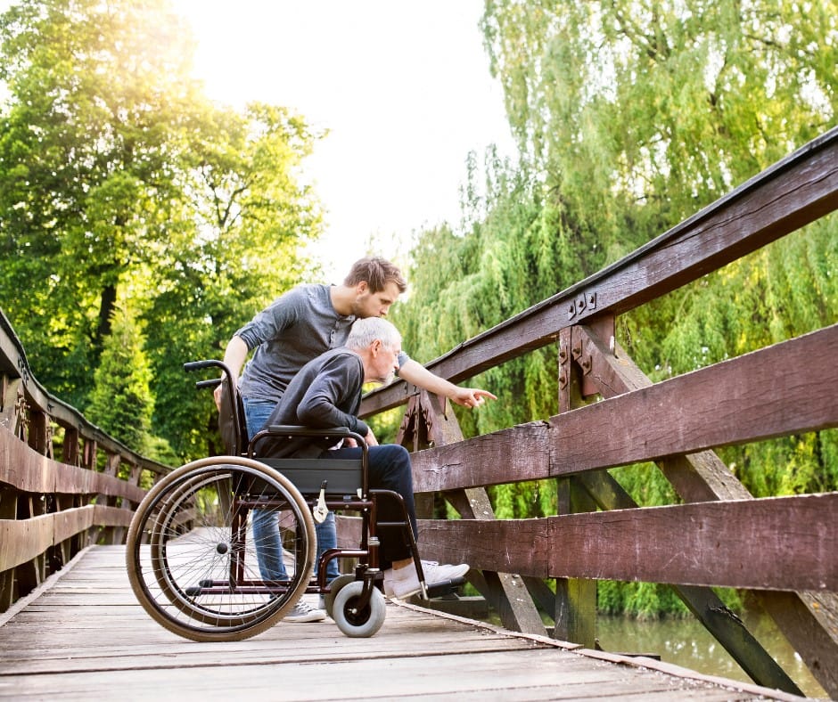 A caregiver helping a resident in a wheelchair on a bridge