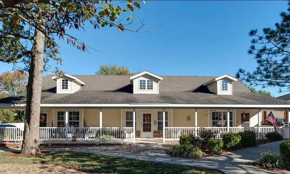 Exterior view of a senior living facility with porch and trees