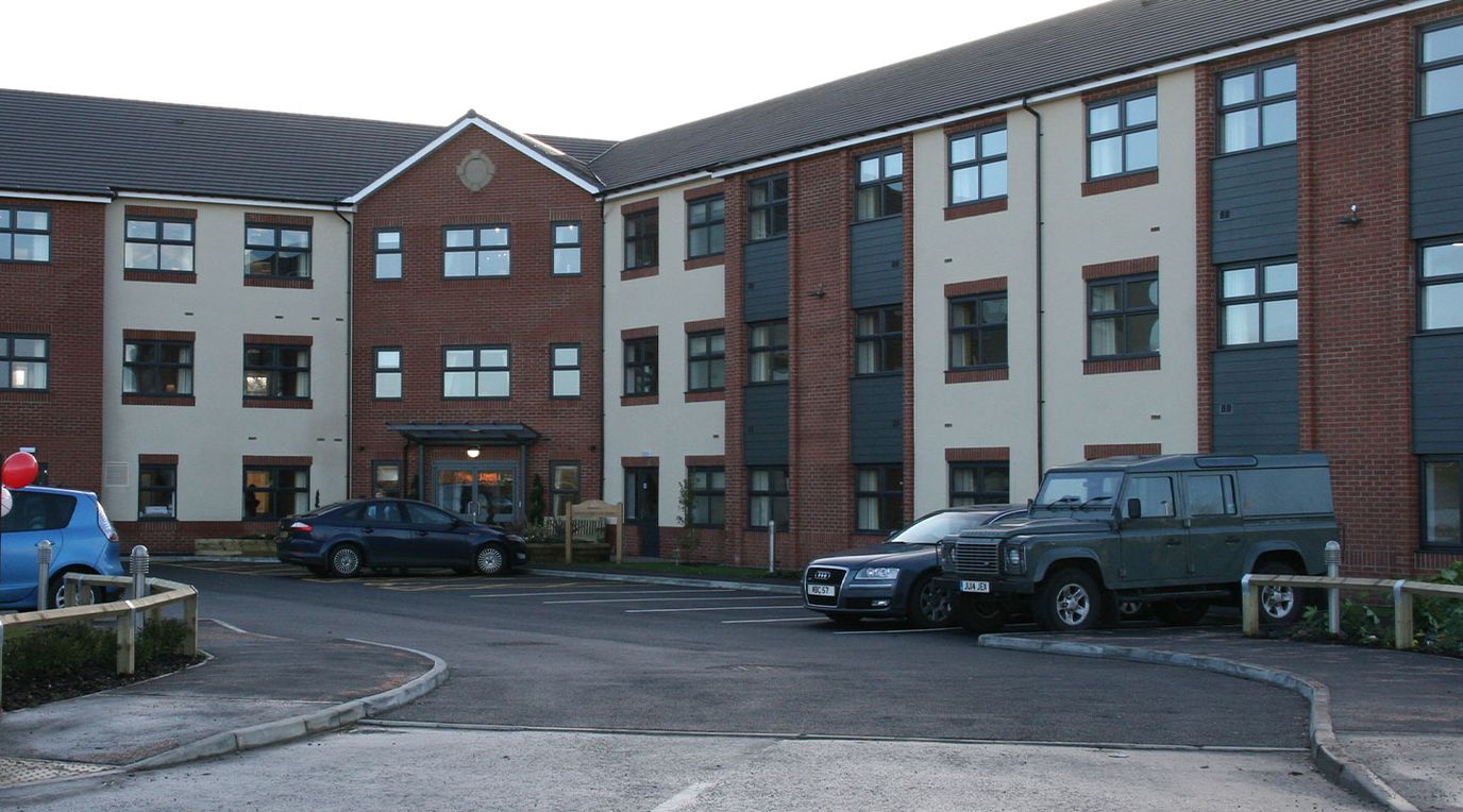 Exterior view of Lostock Lodge Care Home with parking area