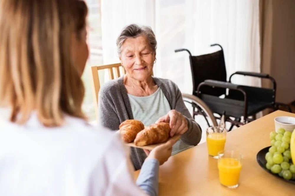 Caregiver serving food to senior woman at a table