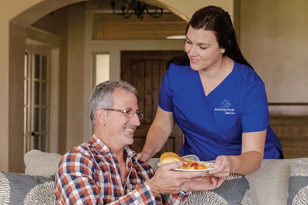 Caregiver serving food to a resident in a cozy living area