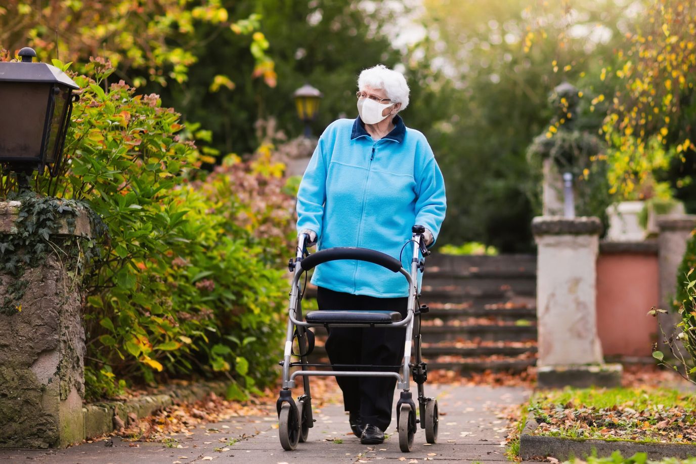 An elderly woman walking with a walker in a garden