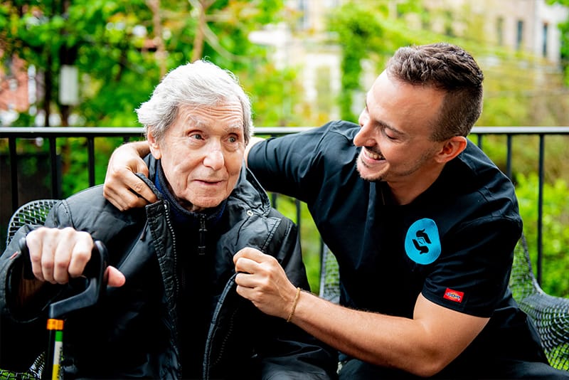 Caretaker assisting an elderly man outdoors.