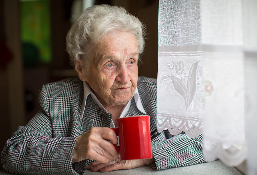 Elderly woman holding a red mug by a window