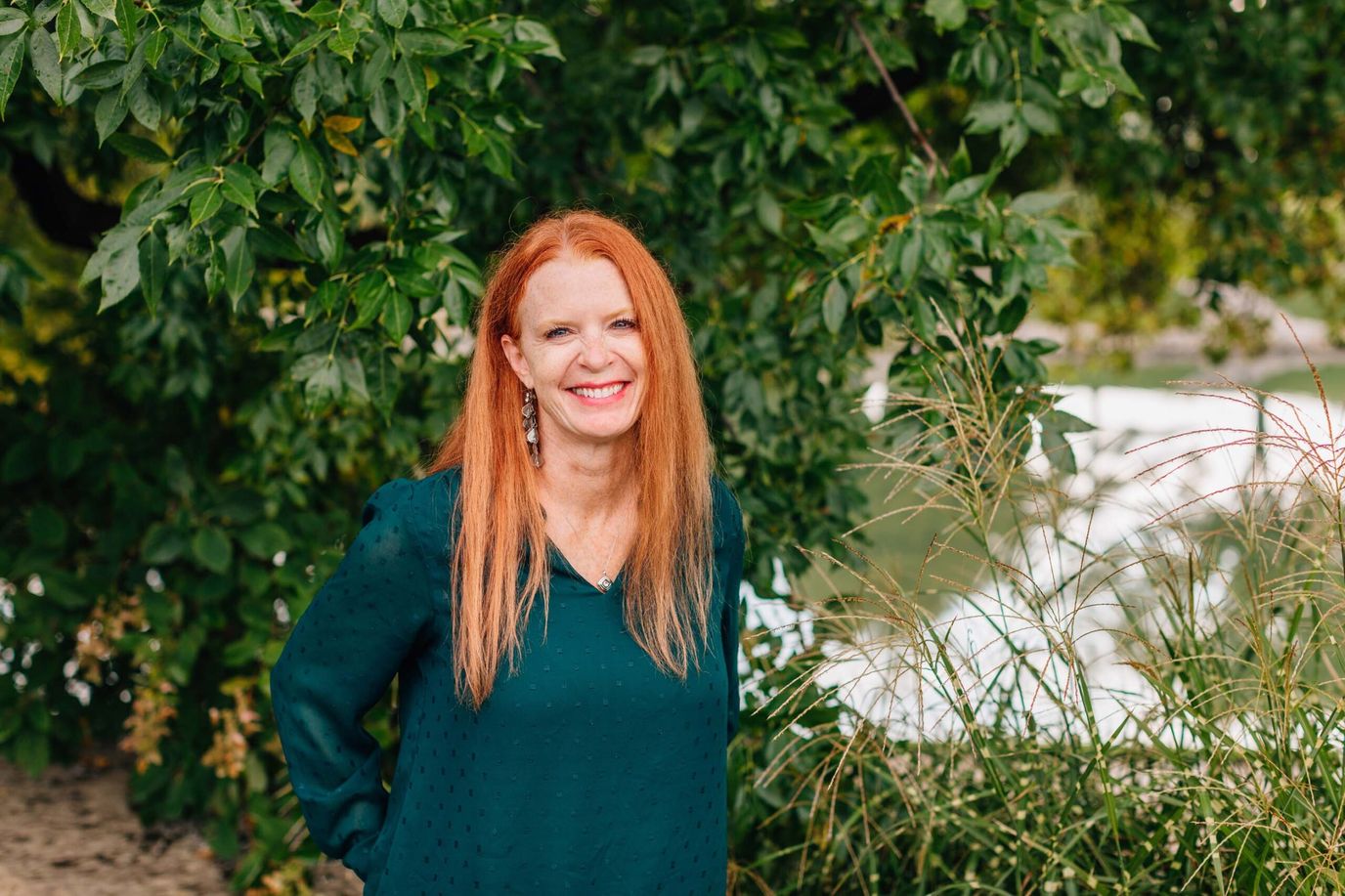 Smiling woman standing outdoors near greenery.