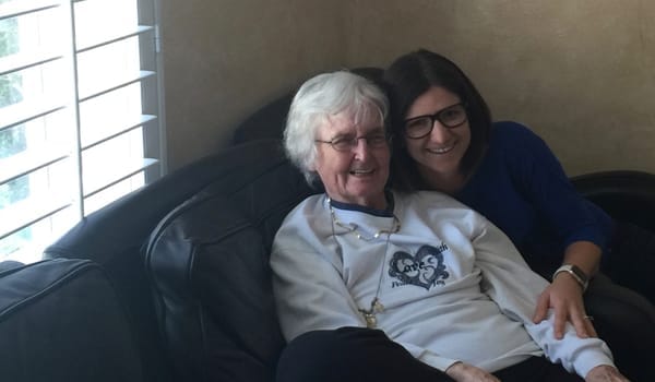 Two women smiling on a couch in a cozy setting.