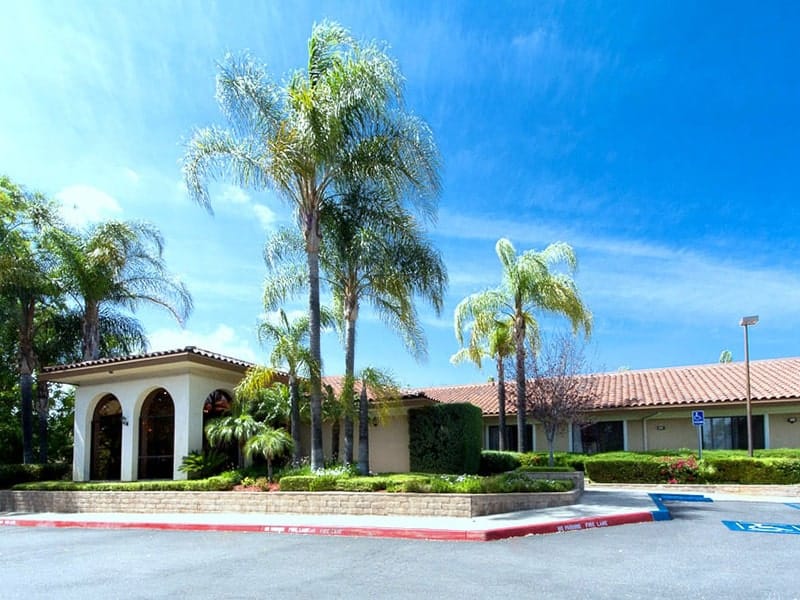 Front view of a senior living facility surrounded by palm trees