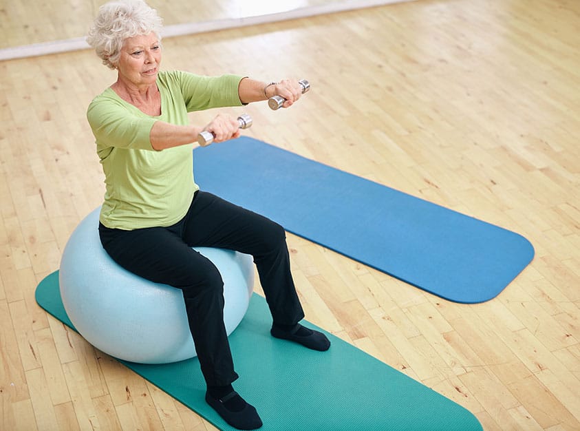 Senior woman exercising with dumbbells on a fitness ball