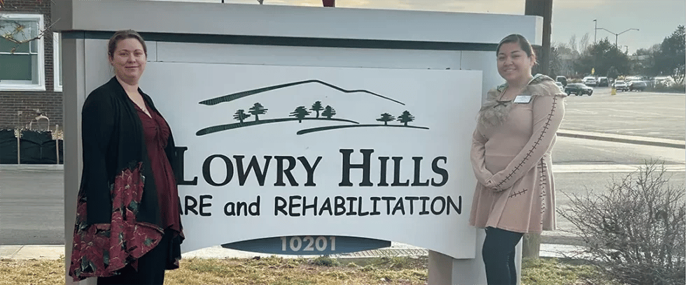 Two staff members posing in front of facility sign