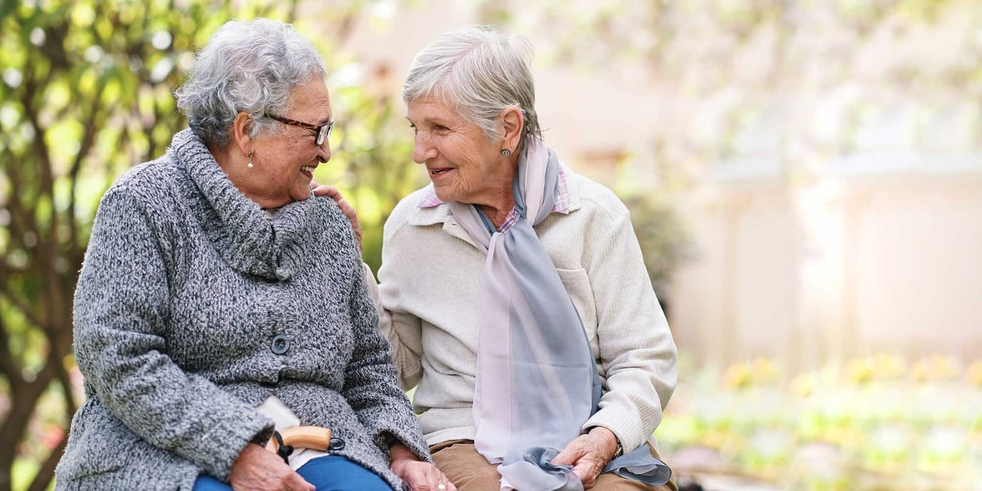 Two elderly women smiling and chatting outdoors