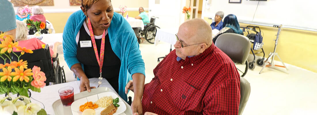 Staff serving a meal to a resident in a dining area