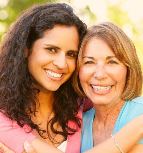 Two women smiling and embracing outdoors