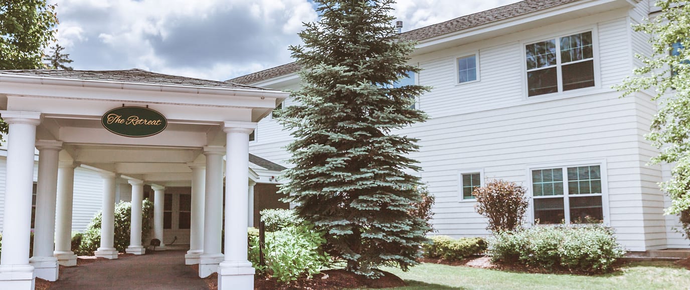 Entrance of The Retreat with landscaping and a pine tree