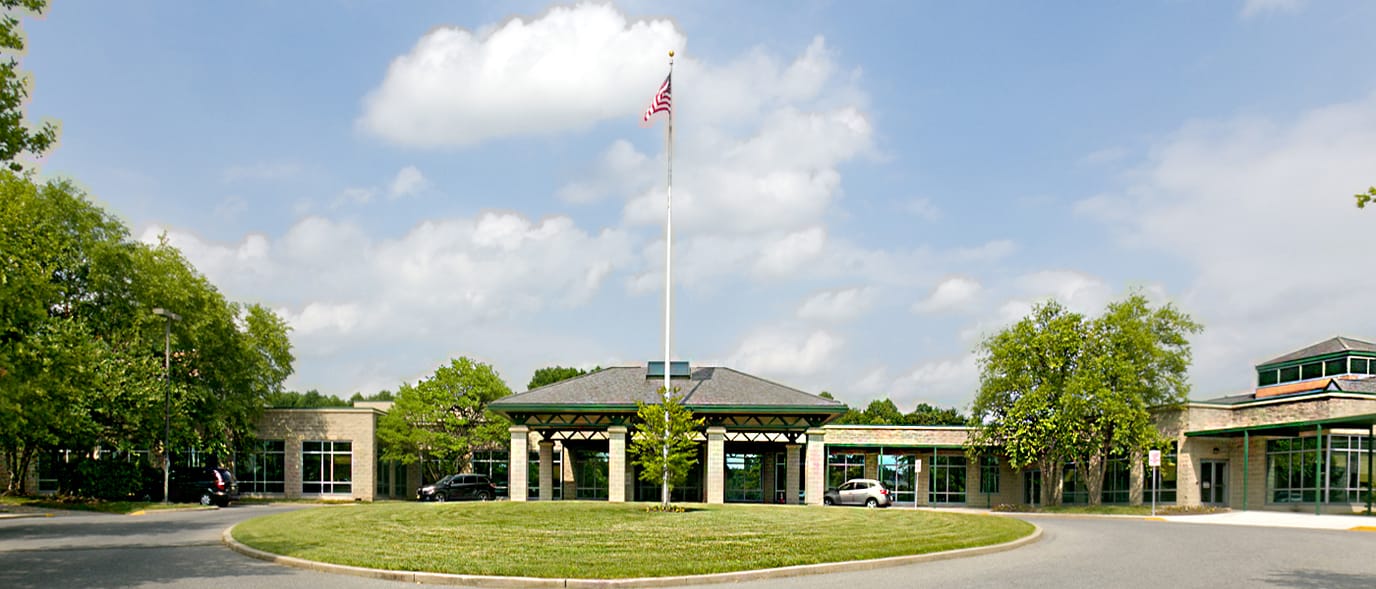 Exterior view of a senior living facility with flag and trees