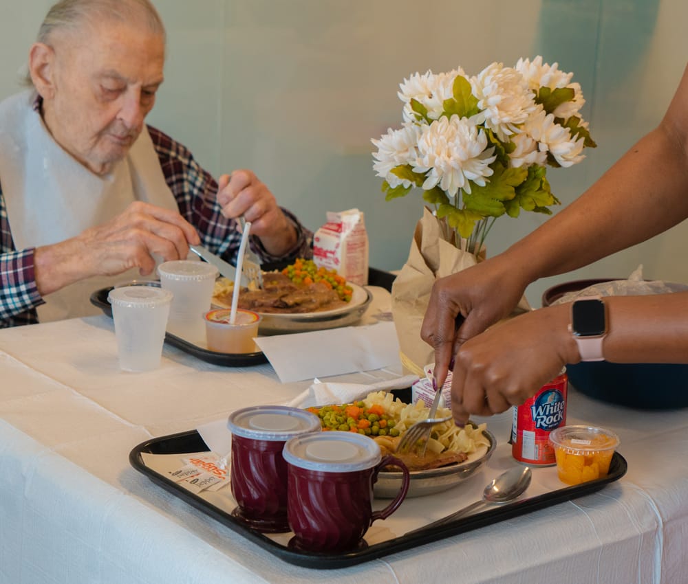 Elderly resident enjoying a meal with staff assistance